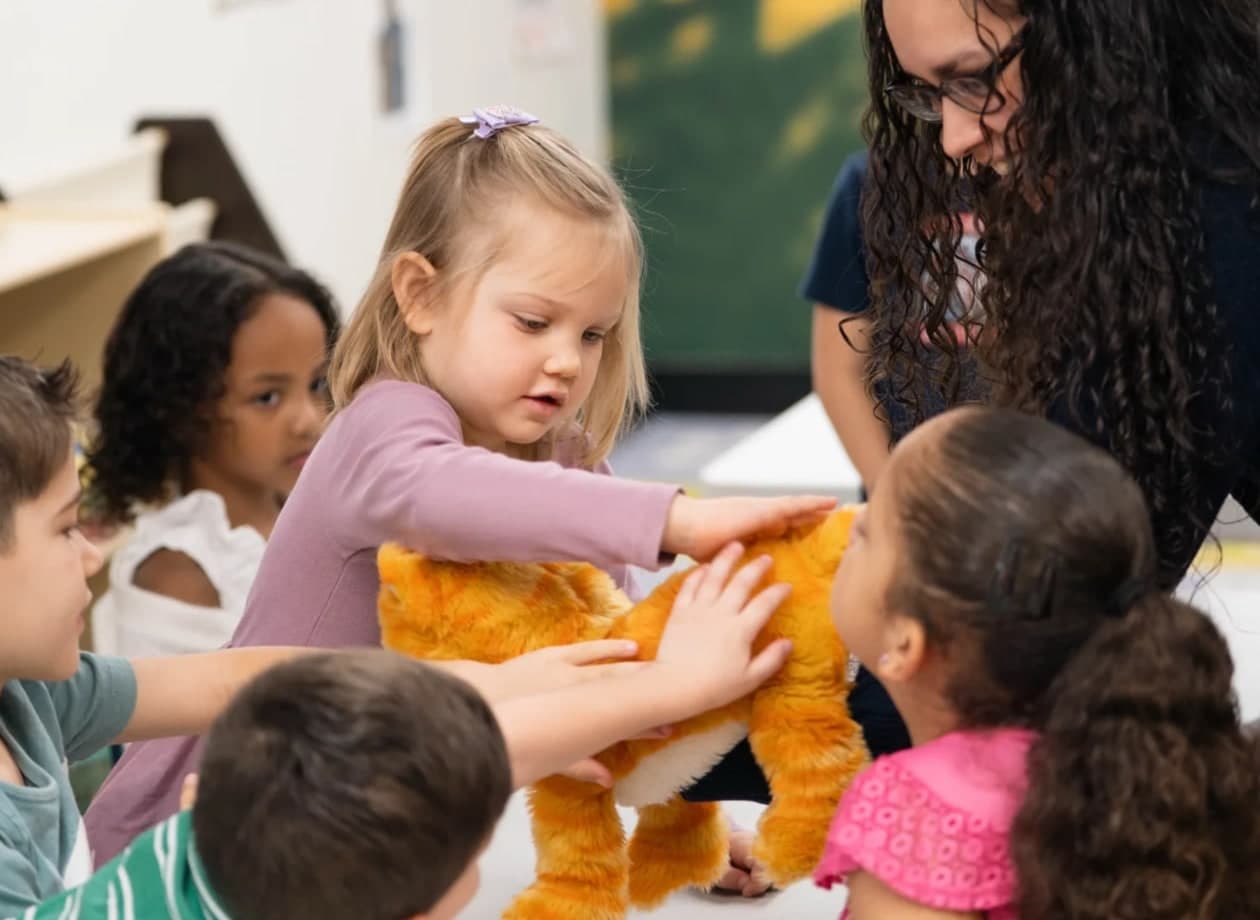 Children and a leader gathered around a plush toy in Victory Kids, from the photography on Victory’s website.